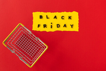 Black friday concept. Top view of yellow torn paper sheet and black friday text in frame on red background. With shopping cart. Composition Black Friday. Vivid colors