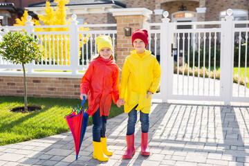 Children with a colorful rainbow umbrella, waterproof jacket and rubber boots.