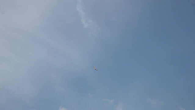 Long shot of flying down small-seat plane with smoke trail in patrially cloudy sky when sunny summer. Aircraft school pilots are training aerobatics