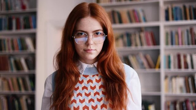 Beautiful red haired girl with freckles reading a book and asking to be quiet with serious look at university library. 