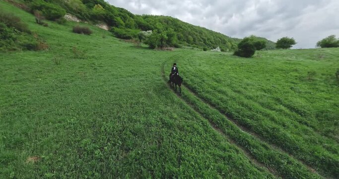 FPV sport drone fly around traditional culture Caucasian horseman with gun travers riding horse at summer mountain valley. Aerial view male equestrian highlander at picturesque dramatic sky rocky 4k
