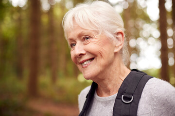 Active Retired Senior Woman Walking In Woodland Countryside Wearing Backpack
