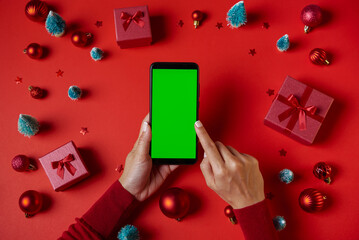 Using Smartphone with blank green screen on table with Christmas decorations. Top view with copy...
