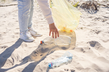 Young female volunteer hand picking up trash, a plastic bottles, clean up beach. Woman collecting garbage. Environmental ecology pollution concept. Earth Day.