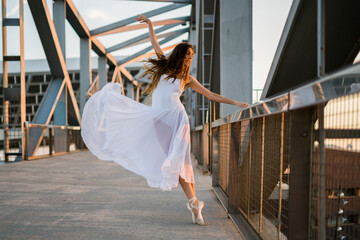 Young adult ballerina dancing on a bridge wearing white dress.