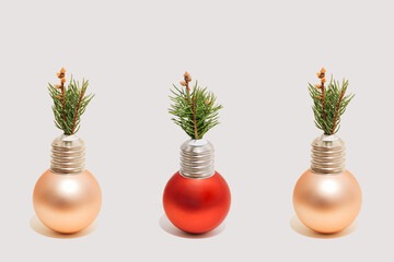 Three ornament Xmas bauble with light bulb cap and a small Christmas tree branch isolated on a white background. New Year greeting card in a minimalist style.