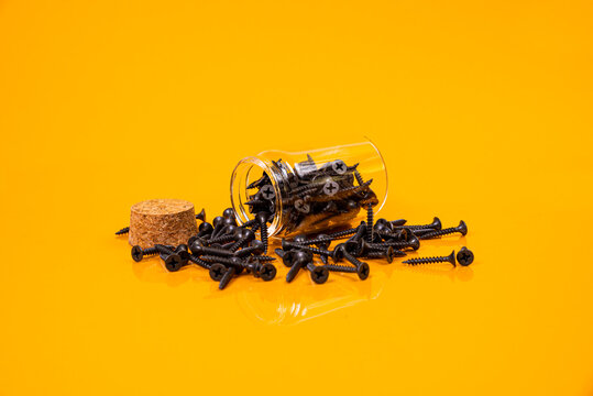 Many metal self-tapping screws made of steel in a glass, in bucket jar. self-tapping screw for metal, for iron, chrome-plated self-tapping screw, on an orange yellow background,