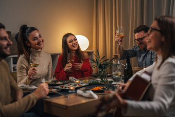 friends celebrating singing and playing guitar at home dinner party