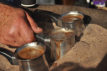 Arabic coffee brewed in a brass metal crucible in hot sand on one of the street stalls in Aqaba, Jordan. Aroma of coffee with cardamom and sugar for 1 Jordanian dinar.