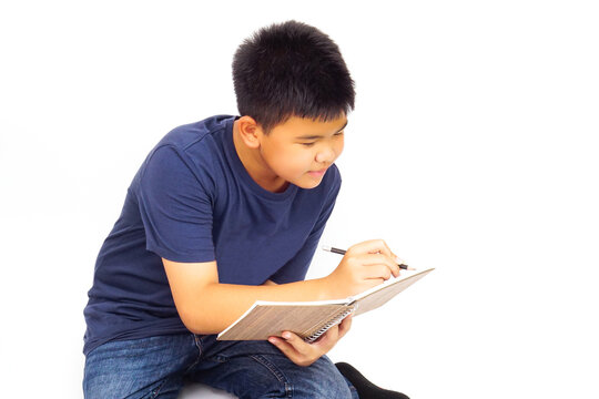 Young boy sitting on white background and writing a book. Education and learning concept.