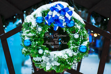 Christmas wreath with fir branches and blue balls, covered in snow. Christmas decor. Street decoration in the winter holiday New Year. with the inscription: "Merry Christmas and Happy New Year".