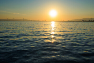Orange sunset sky and sun over the sea. Water surface and outlines on the horizon.