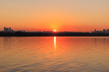 Naklejka premium Orange sunset sky and sun over the sea. Water surface and outlines on the horizon.
