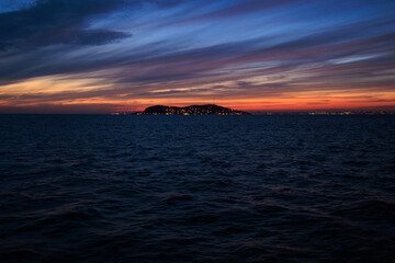 Fototapeta premium Orange sunset sky and sun over the sea. Water surface and outlines on the horizon.