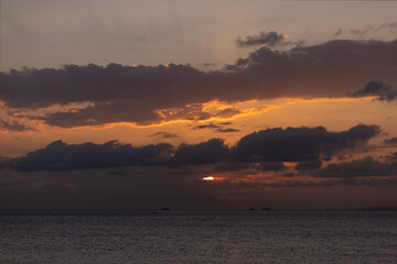 Orange sunset sky and sun over the sea. Water surface and outlines on the horizon.