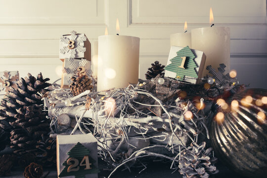 Advent decoration for christmas time. Christmas ornaments with self-made calendar and sustainable natural elements. Candles with white twigs and pine cones in front of vintage background. Close-up.