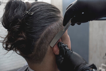 A barber uses a straight edge razor to shave and shape a clients scalp near the temple. Modern...