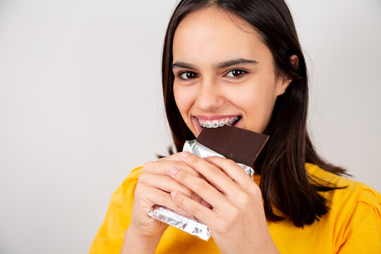  Happy teenager girl with metal orthodontics biting a chocolate bar