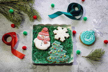 Gingerbreads in the form of snowman, Christmas tree and snowflake in gift box next to pine branch, ribbons and wrapping paper. Christmas and New Year background. Preparing of Christmas gifts. Winter h