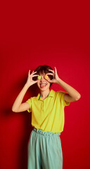 Portrait of cheerful teen girl with curly brown short hair posing with candies isolated over red background. Looking happy
