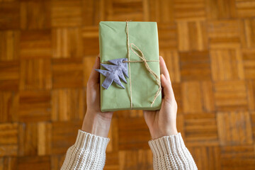 First person top view of woman hands holding craft paper gift box on wooden table