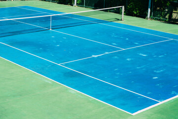 Deserted tennis court with greentrees in background in a public park on a sunny summer morning