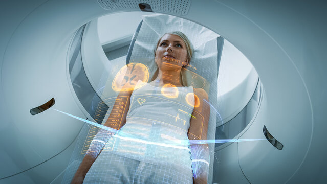 Female Patient Lying On A CT Or PET Or MRI Scan Bed, Moving Inside The Machine While It Scans Her Brain And Vital Parameters. AR Concept With Visual Effects In The Lab With High-Tech Equipment.