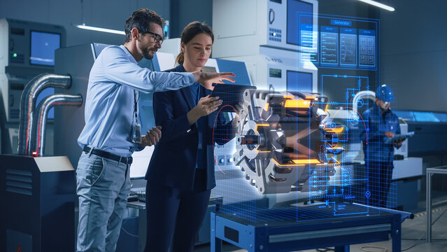 Factory Office Facility: Chief Engineer Holds Tablet Computer, Shows Augmented Reality Model Of An Electric Generator To A Female Project Manager. Modern Industry 4.0 Research And Development Center.