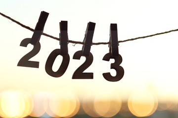 Wooden number hang on rope attached with clothes peg pins over orange morning sky sunrise and blurred city bokeh light background. Happy New Year 2023 celebration for brighter start day concept.