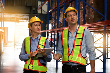 A team of Caucasian male and female engineers stood on a shelf stored in a warehouse. Use radios and clipboards. Check the stock in the warehouse