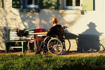 Alter Mann im Rollstuhl sitzt vor seinem Haus in der Abendsonne