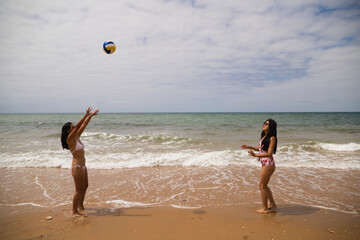 Two young and beautiful women playing boley on the shore of the beach. The women are enjoying the game and their day at the beach in paradise. Holidays and travels.