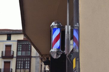Poste de barbero azul, blanco y rojo con cromados y de fondo un edificio