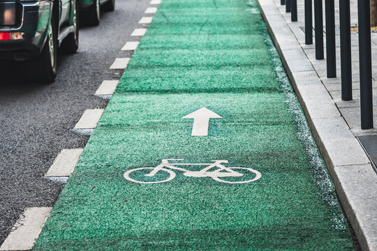 Cars parked next to green bicycle lane with a road mark on it and a white arrow showing direction of circulation