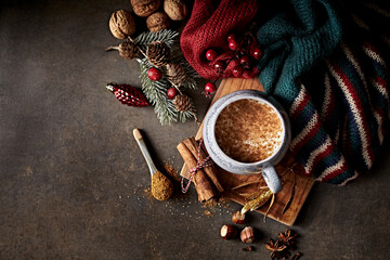 Hot milk with Christmas spices, warm shawl and Christmas decorations on rustic background. Copy...