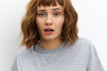 a sweet, inspired, beautiful red-haired, curly-haired woman stands on a white background in a gray cotton T-shirt and looks at the camera with a gentle gaze