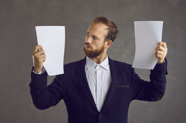 Studio portrait of adult caucasian businessman comparing two document holding in hands....