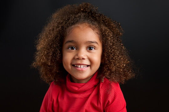 Portrait of smiling little girl wearing red turtle neck on black background
