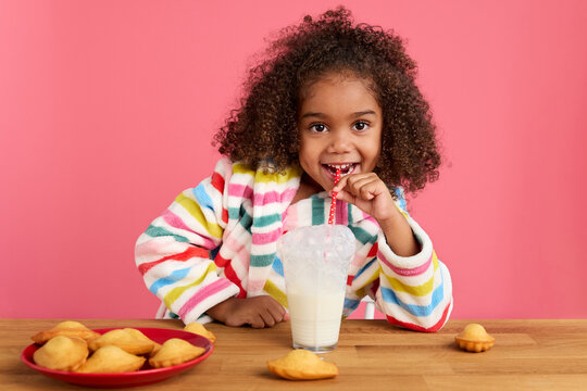 Happy little girl blowing bubbles in glass of milk