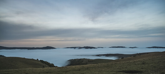 Panorama of mountain hills and rows with low clouds and fog in the valley between the mountains, in the early morning in the mountains