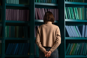 Apathy and frustration. Cognitive overload from an overabundance of news and information noise, concept. Back view of a woman standing with her face buried in bookshelves.