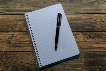 Empty notebook sheet with a pen on wooden background and copy space.