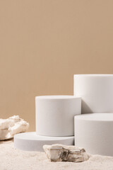 Natural cosmetic background for product presentation. Rocks and white podiums on the sand. Front view.
