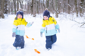 Fototapeta na wymiar Happy twins brothers boys playing with snow in winter nature. Children having fun outdoors