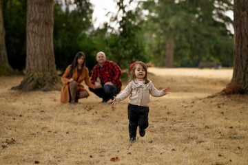 A cute little girl is playfully running away from her parents in a beautiful autumn colored park