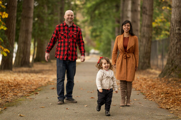 Fototapeta premium A cute little girl is playfully running away from her parents in a beautiful autumn colored park