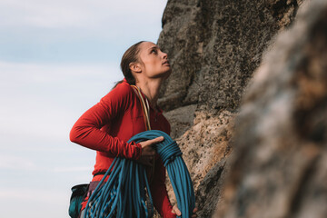 A woman in a red shirt rock climbing on a sunny day.