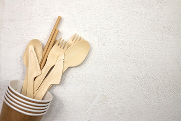 Disposable bamboo cutlery in disposable paper cups on a gray background. Top view, place for text.