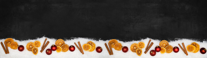 Fototapeta premium Christmas advent celebration holidays background banner panorama greeting card - Frame made of ornaments, red baubles, orange slices, cinnamon sticks and snow on concrete table, top view