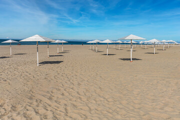 Fototapeta premium sunny sandy beach with numerous white wooden umbrellas against a blue cloudy sky